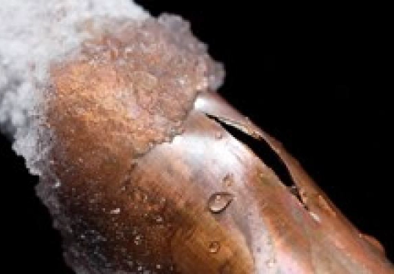 Frozen copper water pipe split open by pressure, with ice on the pipe
